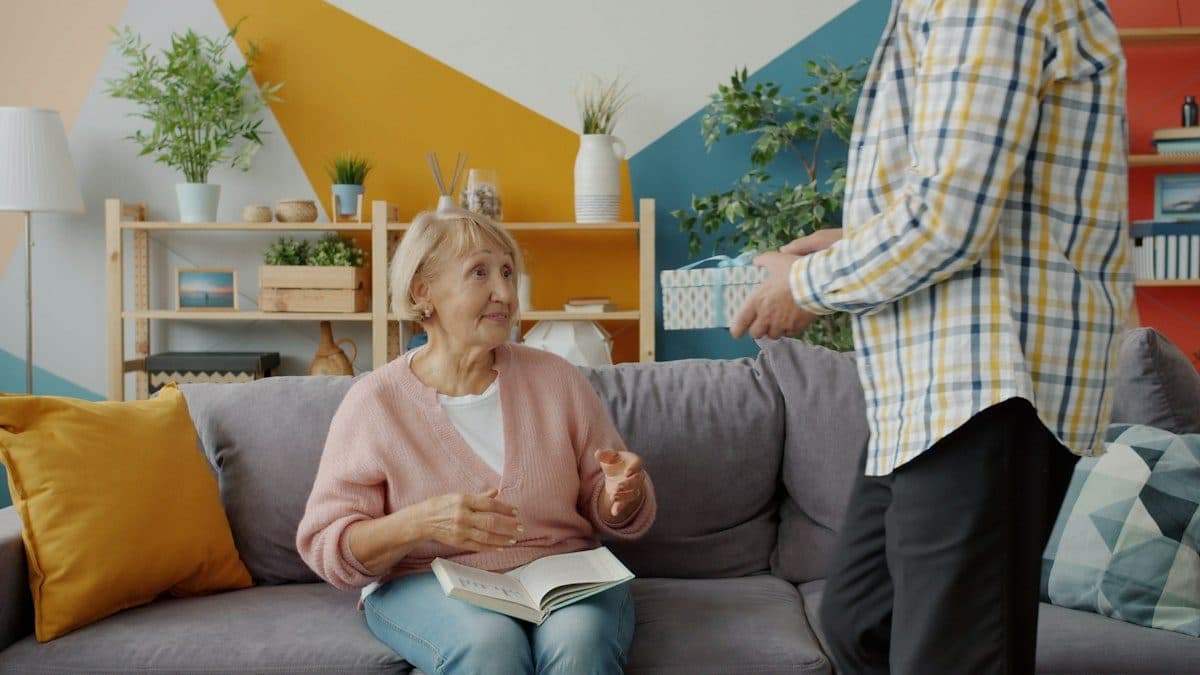A senior woman on her couch smiling up at a visiting family member